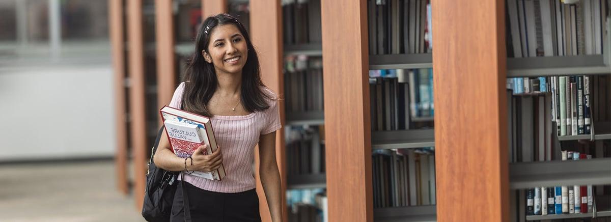 Smiling woman walking through library holding a book